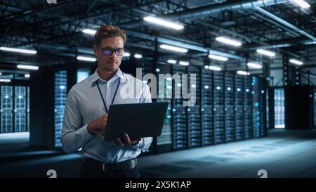 Technology Research Facility: Male Project Manager Standing at the Corridor and Uses Tablet Computer. Engineers or Developers Work on Engine Design and Use Digital Computers Stock Photo