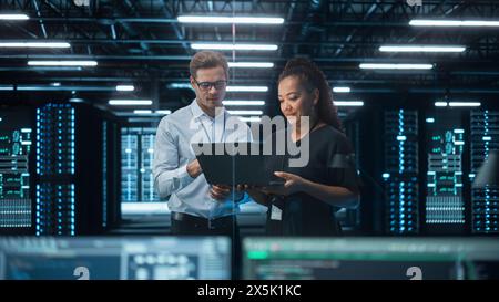 Senior CEO Talking to Young Confident Manager while Using Computer in Modern Office. Colleagues Discuss Commercial, Financial and Marketing Projects. Specialists Work in Diverse Team. Stock Photo
