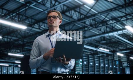 Successful Businessman Using Laptop Computer, Standing in Modern Dark Office Working on Financial, Business and Marketing Projects. Low Angle Portrait of Caucasian Manager Stock Photo