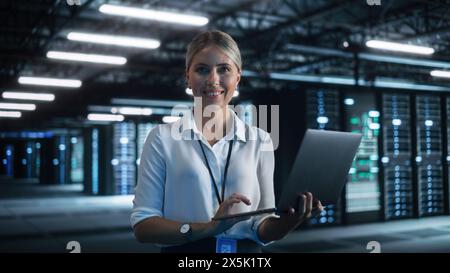 Cheerful Blonde Female IT Specialist Using Tablet Computer in Data Center, while Smiling to the Camera. Successful Businesswoman, e-Business Entrepreneur Concept Stock Photo