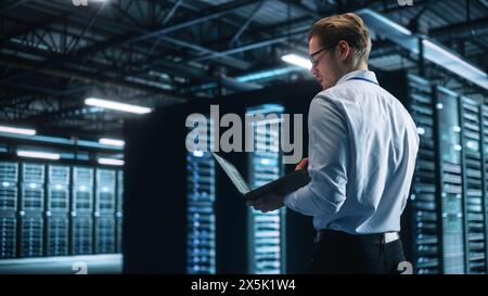 Data Center Male It Specialist Using Laptop while Working on Computer. Information Technology Professional. Server Farm Cloud Computing and Cyber Security Maintenance Concept Stock Photo