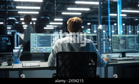 IT Specialist Uses Computer in Data Center. Server Farm Cloud Computing Facility with Male Maintenance Administrator Working During the Evening. Cyber Security and Network Protection. Stock Photo