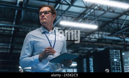 Late at Night in Private Office Businessman Looking Away while Works on a Laptop. Succesful Businessman and e-Business Entrepreneur Overlooking Server Farm Cloud Computing Facility Stock Photo