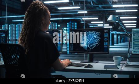 Female Information Technology Specialist and Data Center Administrator Working on her Computer, Monitoring Web Services, SAAS, Cloud Computing Facility, Performing Maintenance and Cyber Security Stock Photo