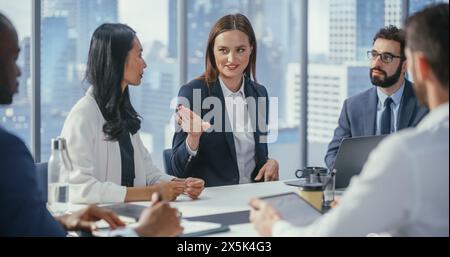 Modern Multi-Ethnic Office Conference Room Meeting: Ambitious Beautiful Caucasian Businesswoman Presenting Investment Strategy to Partners, Pitching Investment Strategy. Diverse Team Businesspeople Stock Photo