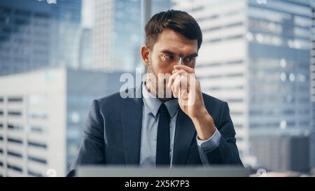Businessman in a Suit Sitting at a Desk in Modern Office, Using Laptop Computer. Thinking About a Good problem Solving Solution. Successful Finance Manager Planning Work Projects. Stock Photo