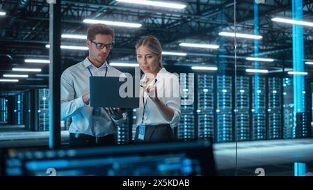In Technology Research Facility: Female Project Manager Talks With Chief Engineer, they Consults with Each Other. Team of Industrial Engineers, Developers Work on Engine Design Using Computer Stock Photo