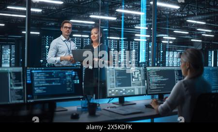 Female e-Business Entrepreneur and Male IT Specialist Discussing Something and Use Laptop in Big Data Center Server Room. Work on Web Services Cloud Computing SAAS Concept Stock Photo