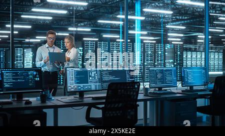 IT Specialists Using Laptop Computer in Data Center. Male Technician and Female e-Business Entrepreneur Overlooking Server Farm Cloud Computing Facility Together Stock Photo