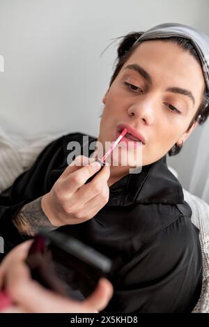 Young relaxed glamorous male in black bathrobe applying pink lipstick on lips. close up portrait. lifestyle, free time, spare time Stock Photo