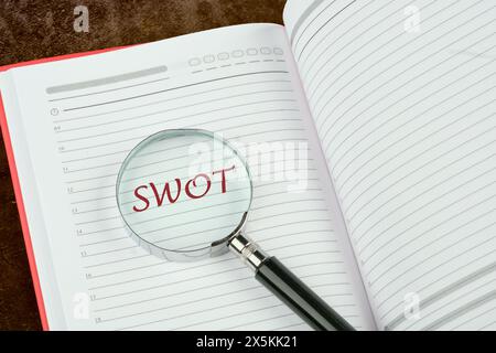 SWOT Strengths Weaknesses Opportunities Threats written through a magnifying glass in the notebook of a businessman, manager, teacher Stock Photo