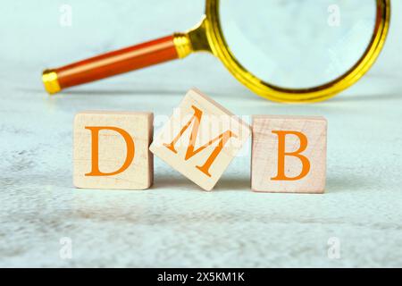 DMB text on wooden cubes with a magnifying glass in the background Stock Photo