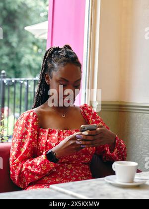 Smiling woman in red dress holding smart phone at cafe table Stock Photo