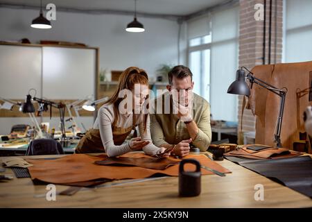 Two young leather craftsmen make decision, talk, discuss while working in the workshop Family small business. Stock Photo