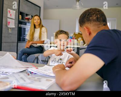 Father assisting son doing homework at home, mother in background Stock Photo