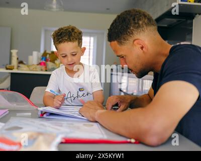 Father assisting son doing homework at home Stock Photo