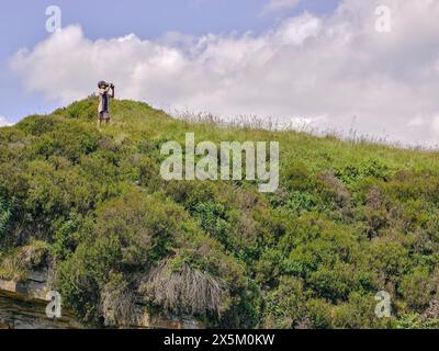 Boy standing on top of hill and looking through binoculars Stock Photo