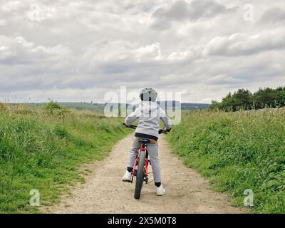 Rear view of boy riding bicycle in countryside Stock Photo