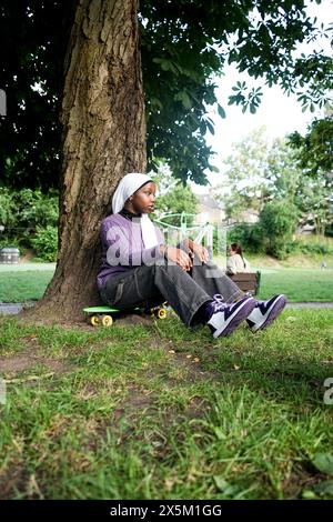 UK, London, Young woman wearing hijab sitting on skateboard in park Stock Photo