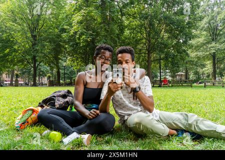 USA, Couple sitting on lawn in park, looking at smart phone Stock Photo