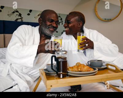 UK, Mature couple enjoying breakfast on bed in hotel room Stock Photo