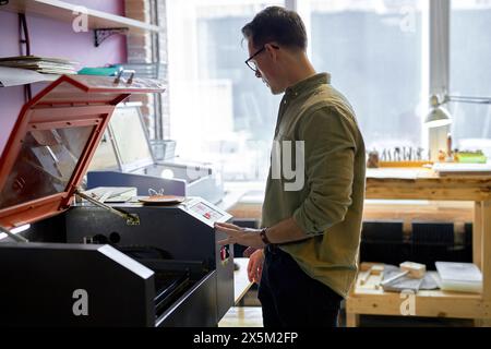 leathe crafting with laser engraving machine, close eup side view shot. copy space, guy learns to work with 3D printer Stock Photo