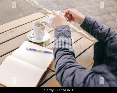 UK, Close-up of womans hands pouring tea at outdoor table Stock Photo