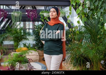Portrait of woman wearing headscarf standing in room full of houseplants Stock Photo