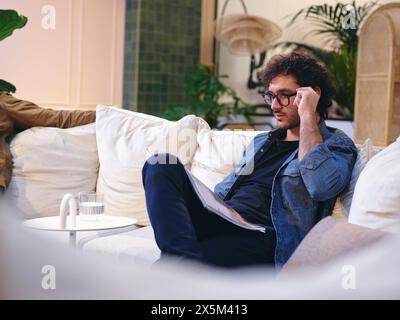 UK, London, Man reading magazine on sofa in modern office lobby Stock Photo