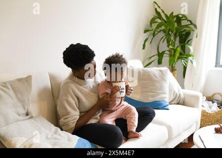 Mother and daughter relaxing on sofa and drinking tea Stock Photo