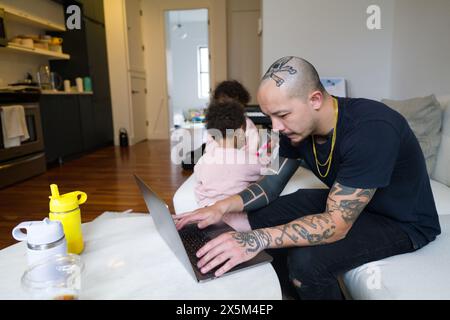 Father working on laptop while daughters playing Stock Photo