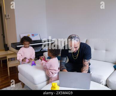 Father working on laptop while daughters playing Stock Photo