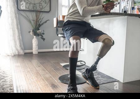 Low section of man with prosthetic leg using smart phone in kitchen Stock Photo
