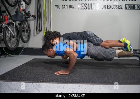 Man with prosthetic leg doing push-ups in gym with son on back Stock Photo
