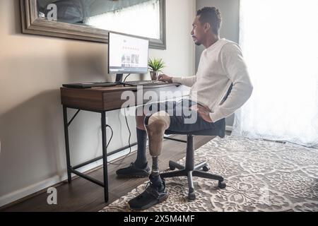 Man with prosthetic leg using computer at home Stock Photo