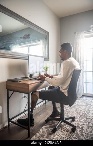 Man with prosthetic leg using computer at home Stock Photo