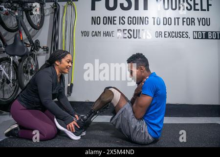 Woman assisting man with prosthetic leg doing sit-ups in gym Stock Photo
