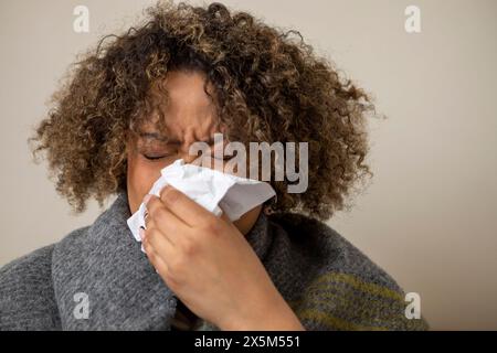 Woman wrapped in blanket blowing nose Stock Photo