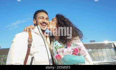 Woman with bouquet kissing smiling man outdoors Stock Photo