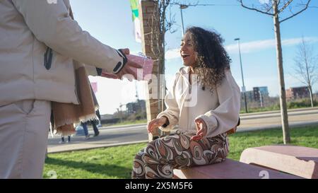Man giving gift to smiling woman sitting on bench Stock Photo