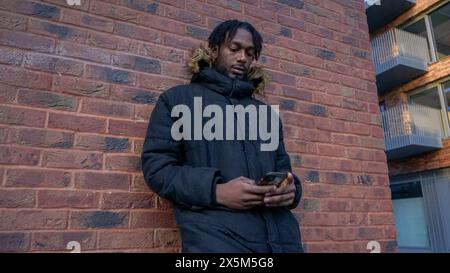 Young man leaning against brick wall, looking at smart phone Stock Photo
