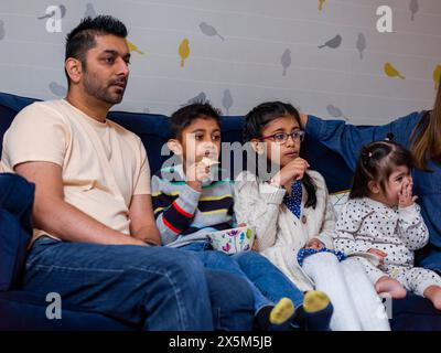 Parents with children sitting on sofa and watching TV Stock Photo