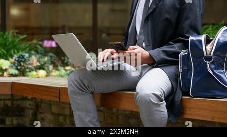 Midsection of business man using laptop and mobile phone Stock Photo