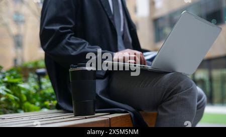 Midsection of business man sitting on bench and using laptop Stock Photo