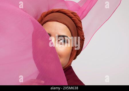 Studio portrait of woman wearing brownhijab surrounded with pink fabric Stock Photo