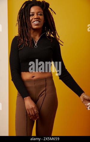 Studio portrait of smiling woman with dreadlocks against yellow background Stock Photo