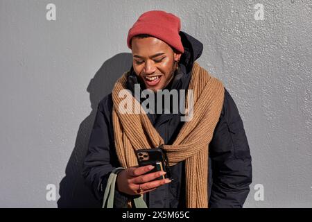 USA, New York City, Smiling queer man in warm clothing looking at smart phone Stock Photo