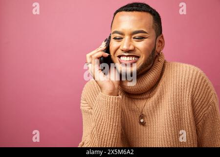 Studio shot of smiling queer man talking on smart phone Stock Photo