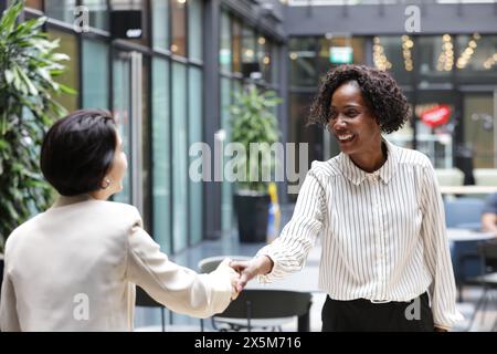 Smiling businesswomen shaking hands in office Stock Photo