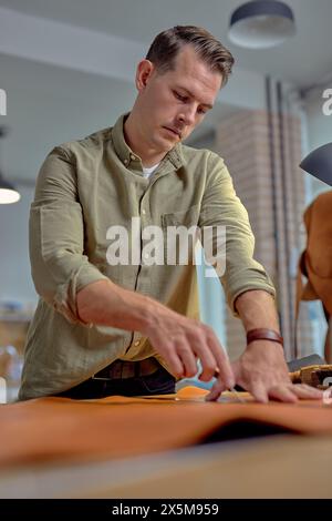Close up side view hardworking artisan working with natural leather and tools. Handmade master at work in local workshop.blurred foreground Stock Photo